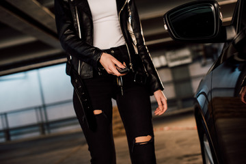 Fototapeta na wymiar cropped view of woman holding key in parking near black automobile