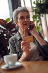 Careful aged woman talking by phone in cafe