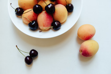 apricots and cherry in a plate on a light background