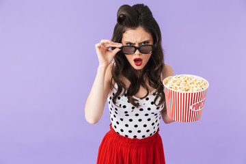 Portrait of gorgeous pin-up woman 20s in retro polka dot dress and 3D glasses holding bucket with...