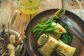 traditional German cuisine, delicious, baked Maultaschen with spinach sauce and green legumes, next to it stands a glass of hot broth of beef