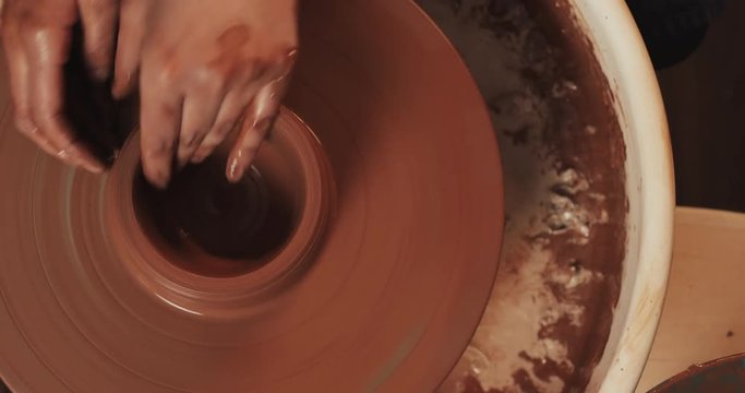 Potter makes pottery from clay close up. Making ceramic products from red clay. Twisted potter's wheel. Man hands making clay jug. Handmade, craft. Top view.
