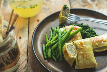 traditional German cuisine, delicious, baked Maultaschen with spinach sauce and green legumes, next to it stands a glass of hot broth of beef