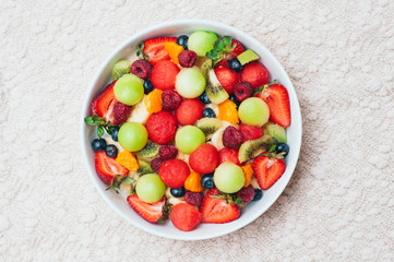 Healthy fresh fruit salad in bowl. Slices of strawberry, raspberry, kiwi, tangerines, blueberry on plate. Delicious fruits. Vegeterian dish. Ripe berries.