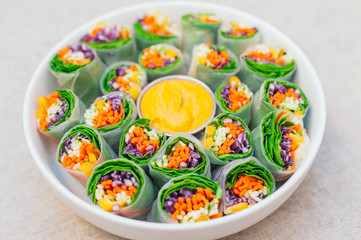 Vegan food concept. Tasty green spring rolls made of rice paper and spinach, filled with fresh chopped vegetables. Small plate with yellow curry sauce in middle