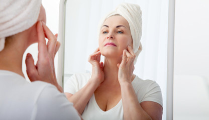 Forty years old woman looking at wrinkles in mirror. Plastic surgery and collagen injections. Selective focus on the face.
