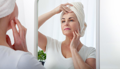 Middle aged woman looking at wrinkles in mirror. Plastic surgery and collagen injections. Makeup. Macro face. Selective focus on the face.