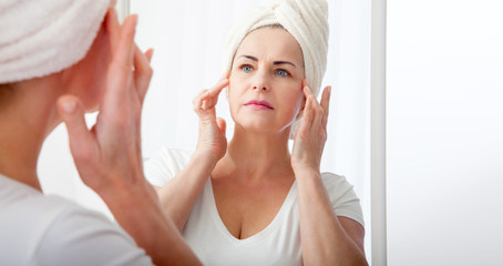 Smiling middle aged woman satisfied with her nature beauty. Cosmetic facial care concept