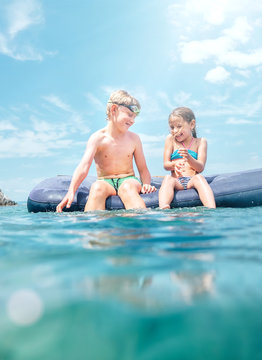 Sister and brother sitting on inflatable mattress and enjoying the sea water, cheerfully laughing when swim in the sea. Careless childhood time unusually unerwater camera shot image.