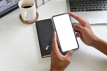 Cropped shot hands using mockup smartphone on office desk with clipping path.