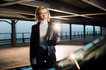 Obraz premium blonde young woman in glasses standing in parking with key near car