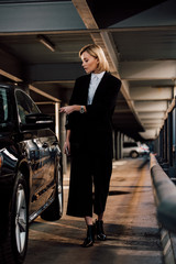 Fototapeta na wymiar attractive blonde woman standing near black automobile in parking