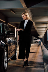 attractive blonde woman standing near black automobile in parking