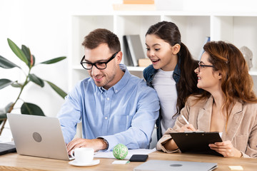 cheerful kid looking at laptop near father and mother in glasses