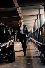 attractive blonde girl walking in parking with key near black automobile