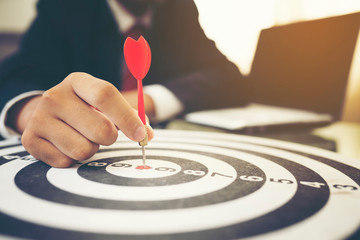 Businessman holding dart arrow hit in target center of dartboard, successful business concept