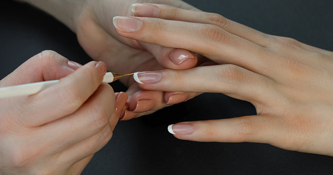 the manicurist paints the client's nails with white nail polish on a black background  Painting nails. French manicure.