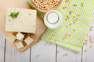 Flat lay of Non-dairy alternatives Soy milk or yogurt in glass bottle and tofu on white wooden table with soybeans in bowl aside