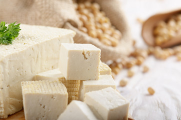 Soy Bean curd tofu on cutting board and in hemp sack on white wooden kitchen table. Non-dairy alternative substitute for cheese