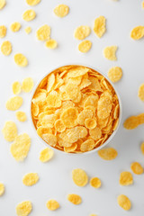 White cup with golden corn flakes, isolated on white background. Hopya crumbled around the cup. View from above