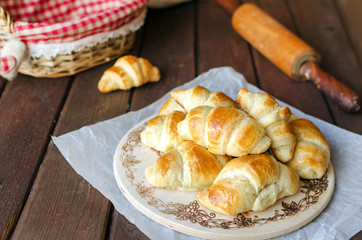 Freshly baked croissants on wooden cutting board on dark wooden table.