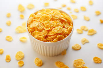 White cup with golden corn flakes, isolated on white background. Hopya crumbled around the cup. View from above
