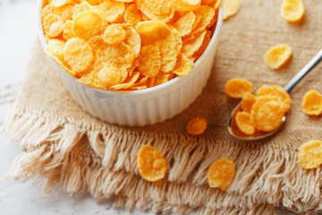 Bowl with golden flakes on a linen, on a light wooden table, next to a spoon. Rustic country style. View from above