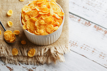 Bowl with golden flakes on a linen, on a light wooden table, next to a spoon. Rustic country style. View from above