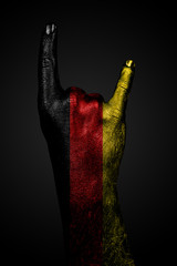 A hand with a drawn Germany flag shows a goat sign, a symbol of mainstream, metal and rock music, on a dark background.
