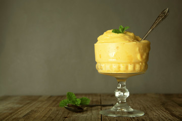 Homemade mango or lemon ice-cream in glass cup, rustic wooden background. Vintage style.