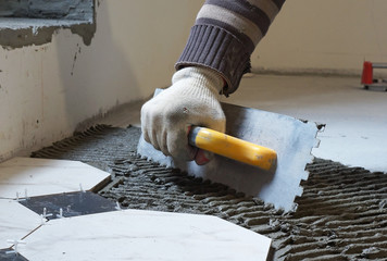Tiler holds the notched trowel and puts tiles adhesive on the floor