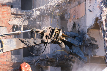Building demolition with hydraulic excavator close-up. Demolished destructed house ruins in european city on bright sunny day. © Arsenii