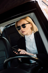 Fototapeta na wymiar attractive blonde girl in sunglasses holding gun in car