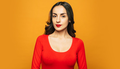 Obraz premium Red velvet. Bodacious girl with a perfect makeup on her face, perfectly curled hair and in cotton red sweater which fits her well in front of orange background.