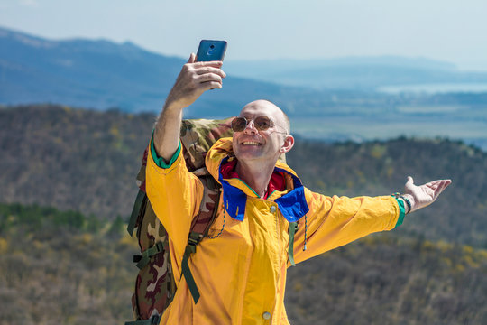 A tourist in a yellow jacket and glasses takes a selfie. In the background mountains. Tourism concept.