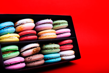 Tasty different colored macarons in black box on red background