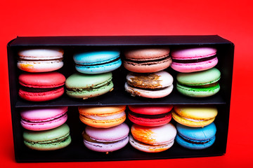 Tasty different colored macarons in black box on red background