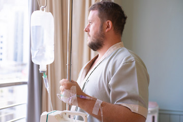 patient with a dropper looks out the window of the hospital room and smiles. back view. Healthcare concept.