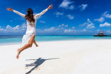 Glückliche Frau in weißem Sommerkleid läuft an einem tropischen Paradies Strand und genießt...