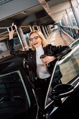 happy girl holding smartphone and disposable cup and waving hand near car