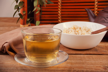 Cooked brown rice in white bowl with chopsticks and cup of green tea on the wooden background.