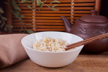 Cooked brown rice in white bowl with chopsticks on the wooden background.