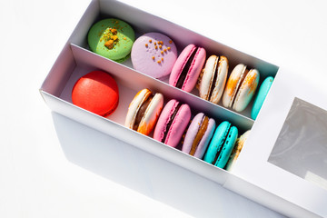 Tasty different colored macarons in white box on light background