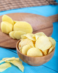 Potato chips and potato on wooden backround.