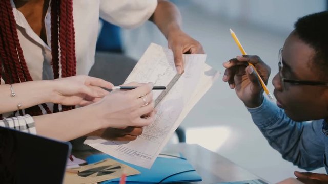 Close-up multiethnic development company colleagues collaborate, brainstorm over project sheet at modern office table.