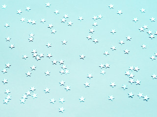 Holiday background with silver star confetti on aquamarine background. Flat lay, top view.