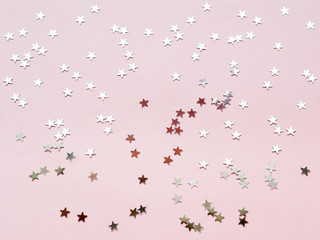 Holiday background with silver star confetti on pink background. Good backdrop for Christmas and New Year cards. Flat lay, top view.