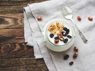 Natural homemade yogurt in a glass jar. Healthy food for breakfast with muesli or granola. Jar with sour cream on linen tablecloth on on wooden table.