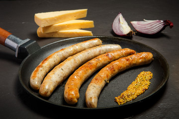 frying pan with five fried thin sausages and granular mustard