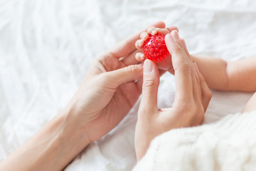 Mother holds newborn baby's hands. Tiny fingers in woman's hand. Red massage ball. Cozy morning at home.